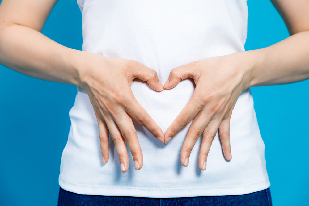 Woman making heart with hands over her stomach.